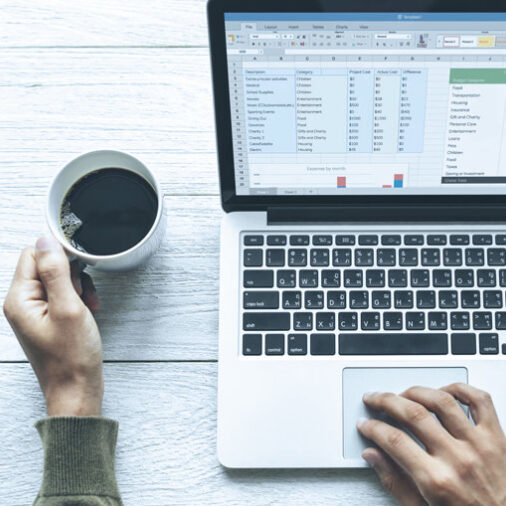 Person holding a cup of coffee while working on a WordPress CMS & WooCommerce Expert Agency WPenabled.com spreadsheet on a laptop at a light wooden table. WPenabled.com